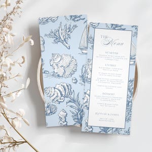 May include: Two-sided wedding menu with a light blue background and a nautical design featuring seashells and sailboats. The menu includes the text "The Menu", starter, entree, and dessert options. The bottom of the menu reads "HANNAH & JAMES" and the date and location.