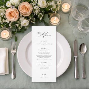 May include: A formal table setting with a white menu card, plate, and silverware. The menu card reads "The Menu" and lists a starter, entree, and dessert. A bouquet of flowers and lit candles are in the background.