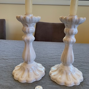 Könnte beinhalten: Zwei weiße Kerzenhalter aus Keramik mit geriffeltem Design und einem gewellten Sockel. Jeder Halter hat eine weiße Kerze.
