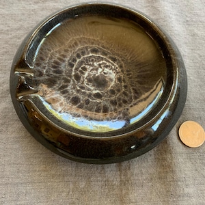 May include: A round, black ceramic ashtray with a brown and white swirl pattern.