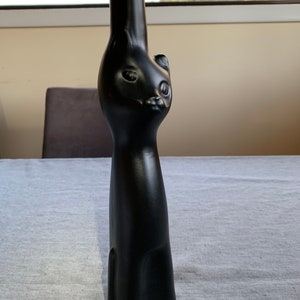 Könnte beinhalten: Eine schwarze Glasflasche in Katzenform. Die Flasche hat einen runden Körper und einen langen, schlanken Hals.
