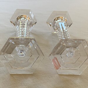 K&ouml;nnte beinhalten: Zwei klare Glaskerzenhalter mit sechseckiger Basis und facettiertem Design. Die Kerzenhalter sind aus Kristall und haben eine polierte Oberfl&auml;che.