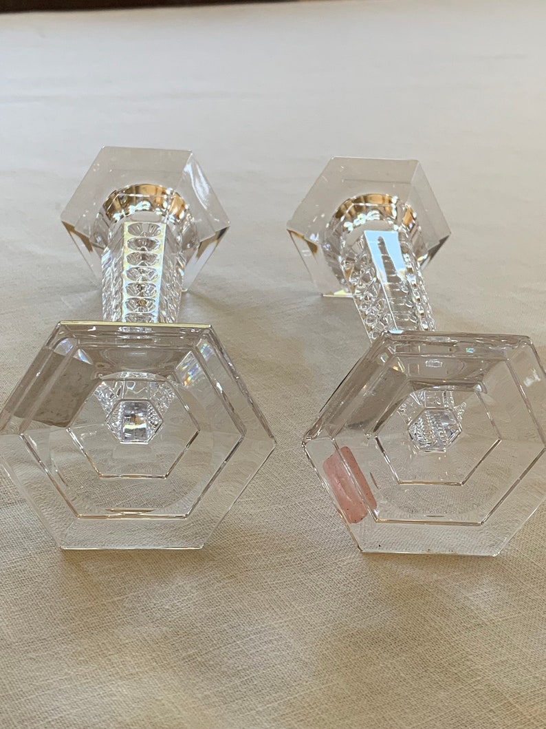 K&ouml;nnte beinhalten: Zwei klare Glaskerzenhalter mit sechseckiger Basis und facettiertem Design. Die Kerzenhalter sind aus Kristall und haben eine polierte Oberfl&auml;che.