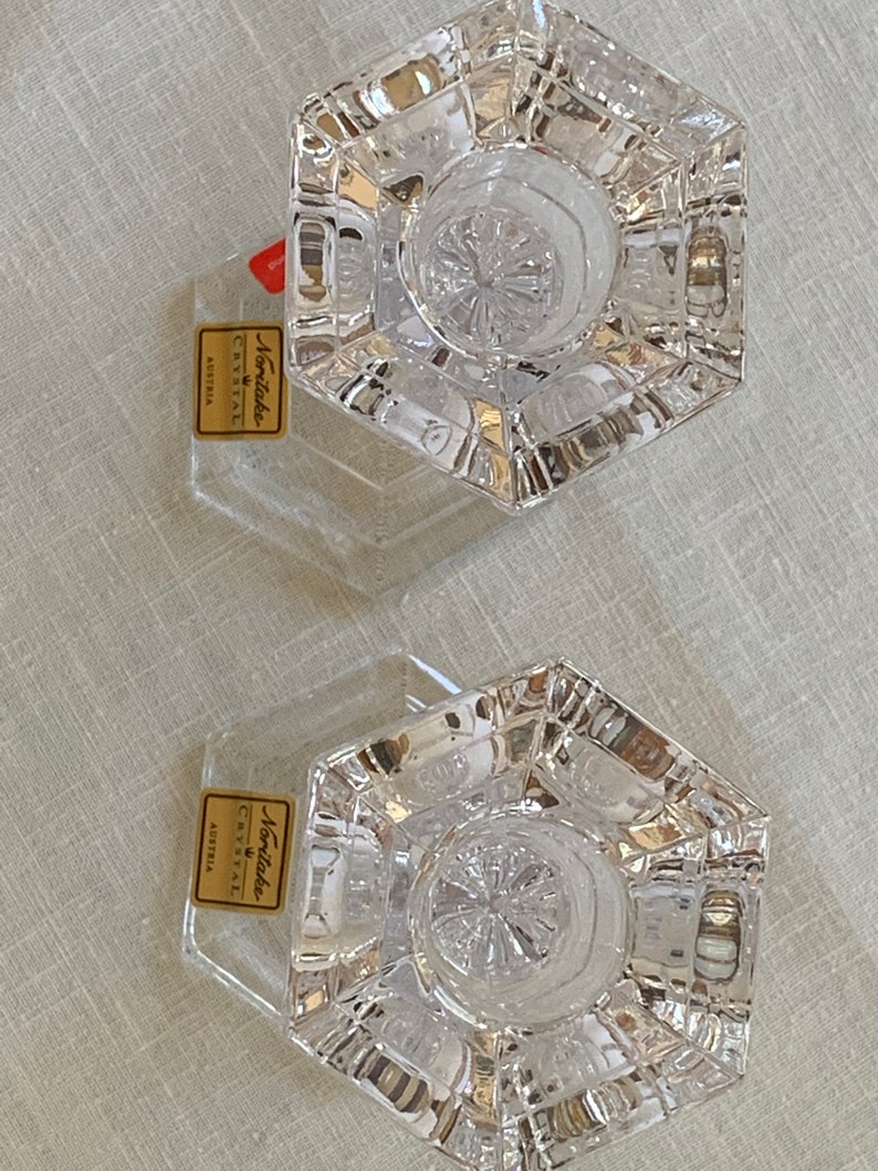K&ouml;nnte beinhalten: Zwei klare Glaskerzenhalter mit sechseckiger Basis und einem Sternmuster. Die Halter werden von Noritake Crystal Austria hergestellt.