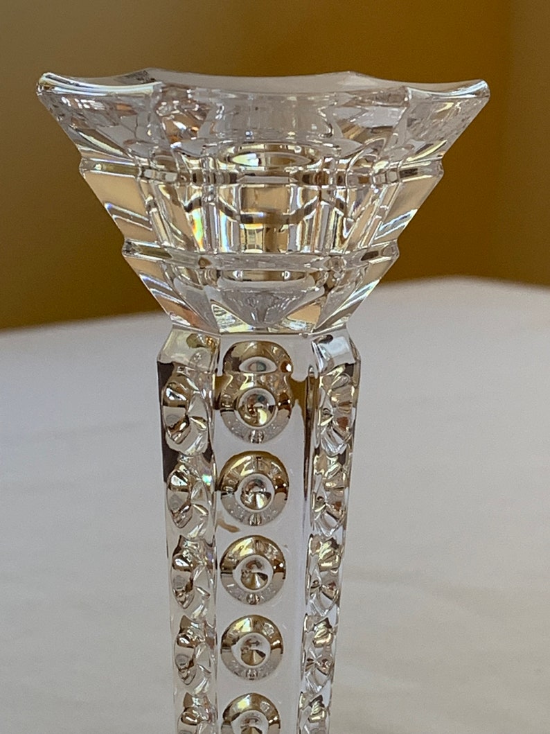 K&ouml;nnte beinhalten: Ein durchsichtiger Glas-Kerzenhalter mit geometrischem Design und einem dekorativen Muster aus Kreisen um die Basis.