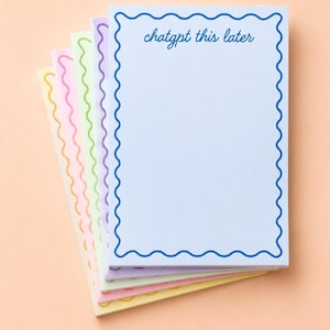 May include: A stack of pastel-colored notepads with scalloped edges. The top notepad is light blue with the text "chatgpt this later" in blue script. The other notepads are pink, green, yellow, and purple.