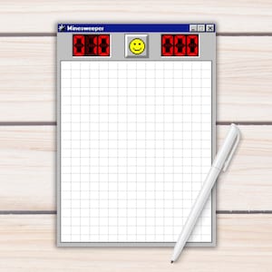 Puede incluir: Un bloc de notas diseñado para parecerse al clásico juego de Windows Minesweeper, con una cuadrícula, una carita sonriente y contadores digitales rojos. Un bolígrafo blanco descansa junto al bloc de notas sobre una superficie de madera clara.