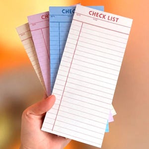 May include: A set of four rectangular paper checklist pads in cream, lavender, blue, and white. Each pad features a header with the text CHECK LIST, a space for a date and title, and a series of horizontal lines for writing tasks in red ink.