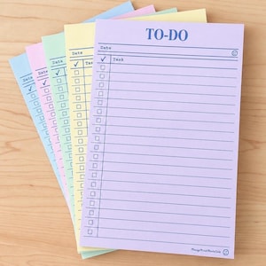 May include: A stack of rectangular to-do list notepads in pastel shades of purple, yellow, green, pink, and blue. Each sheet features the text TO-DO at the top, a date line, a column for checkmarks, and a column for tasks with horizontal lines.