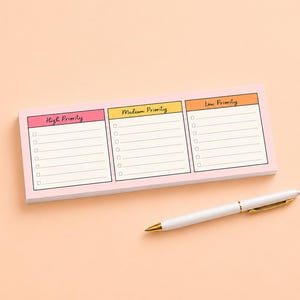 May include: A rectangular notepad with a light pink border featuring three distinct columns labeled High Priority in pink, Medium Priority in yellow, and Low Priority in orange, each with checkboxes and lines, accompanied by a white ballpoint pen.
