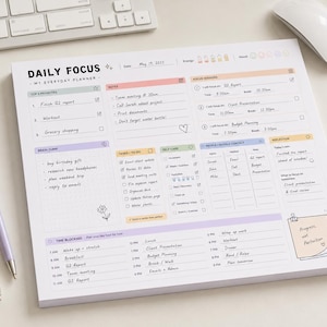 May include: A white daily focus planner notepad with pastel-colored sections for top priorities, notes, focus sessions, brain dump, tasks, self-care, contacts, reflection, and time blocking. The page includes printed text and handwritten entries.