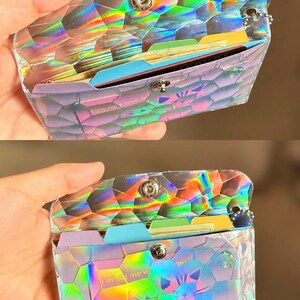 May include: A holographic wallet with a geometric hexagonal pattern and a metallic snap closure. The wallet contains multiple colorful dividers and cards, including one with the visible text 'I'm not me w' and a small circular green logo.