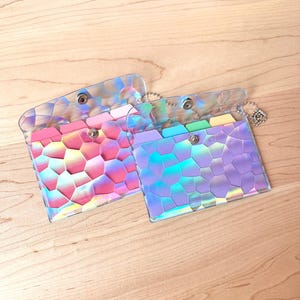 May include: Two small, rectangular, iridescent card holders with a geometric, stained-glass-like pattern. Each holder features a snap-button closure, a metal ball chain attachment, and internal dividers in shades of pink, blue, green, and yellow.