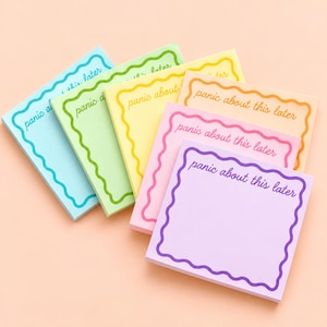 May include: A stack of five square sticky note pads in light blue, light green, yellow, pink, and lavender. Each pad features a wavy border and the text "panic about this later" printed in a cursive font matching the border color.