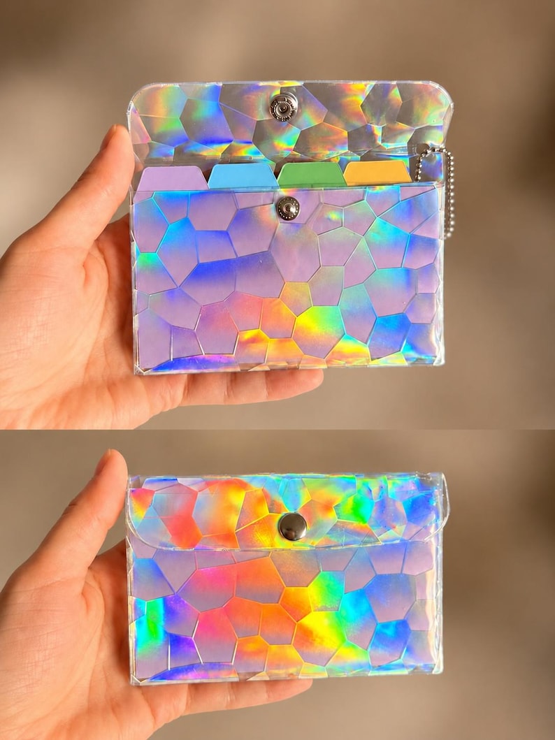 May include: A rectangular holographic card holder with a geometric mosaic pattern that reflects rainbow colors. The accessory features a metal snap button closure, a silver ball chain attachment, and internal dividers in purple, blue, green, and yellow.