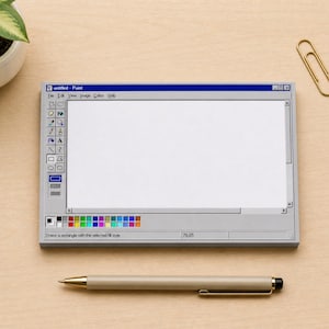 May include: A notepad designed to resemble the classic Windows Paint program interface. The notepad is gray with a blue title bar and a white drawing area. A pen and paperclip are also on the wooden surface.