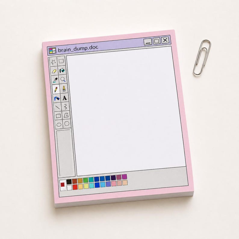 May include: A pink notepad designed to resemble a computer window, with the text "brain_dump.doc" at the top. The notepad features a toolbar on the left side and a color palette at the bottom. A silver paperclip rests on the side.