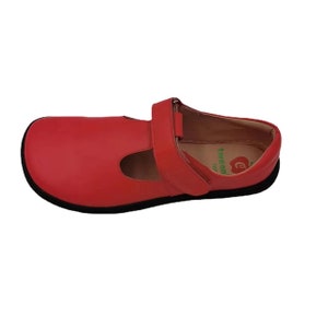 May include: Red leather Mary Jane style shoes with a velcro strap and a black sole. The shoes have a green apple logo with the text "tween" on the inside.