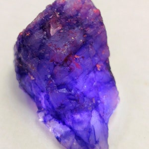 Peut inclure: Un gros cristal d'améthyste violet brut avec quelques inclusions rouges. Le cristal est translucide et de forme irrégulière.