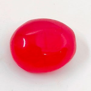 Puede incluir: Una gema roja vibrante y pulida, con una forma suave y redondeada. La piedra tiene una superficie brillante que refleja la luz. La gema se encuentra sobre un fondo blanco, resaltando su color y forma. Para joyería.