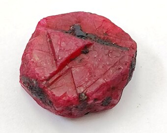 Könnte beinhalten: Ein tiefroter Rubin-Edelstein mit einer rauen, natürlichen Oberfläche. Der Rubin hat eine dreieckige Form und ist von einer leuchtenden, satten roten Farbe.