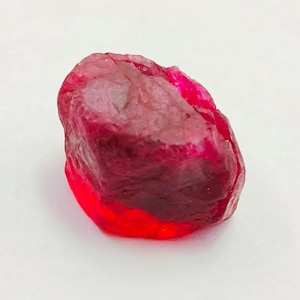 Peut inclure: Une pierre précieuse de rubis naturelle, taillée à l'état brut. Le rubis est d'un rouge profond avec un aspect légèrement translucide. La pierre a une forme irrégulière et une surface texturée, mettant en valeur son état brut et non poli. Le rubis est une pierre précieuse.