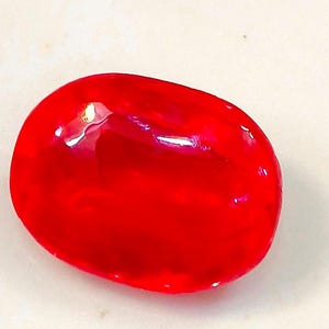 Pode incluir: Uma gema oval de cor vermelha brilhante com uma superfície lisa e polida.
