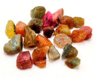 Könnte beinhalten: Eine Sammlung von rohen, ungeschliffenen Edelsteinen in verschiedenen Farben, darunter Rot, Rosa, Gelb, Orange, Grün und Blau. Die Edelsteine sind unregelmäßig geformt und haben eine natürliche, unpolierte Oberfläche.