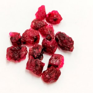 May include: A collection of small, rough, red ruby gemstones. The rubies are various shapes and sizes, and have a deep red color.