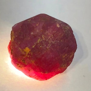 May include: A large, rough, red ruby gemstone with a deep, rich color. The ruby has a natural, unpolished finish and is a beautiful example of this precious stone.