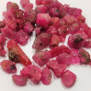 Op de afbeelding: Een verzameling ruwe, roze robijn edelstenen. De robijnen zijn van verschillende groottes en vormen, sommige hebben een iets donkerdere tint.