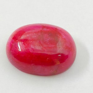 May include: A polished, oval-shaped gemstone in a vibrant shade of red. The surface has a glossy finish, with subtle variations in color and texture. The gemstone is set against a plain white background.