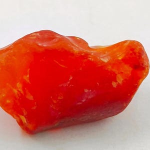 May include: A rough, orange-red gemstone with a translucent, glassy finish.