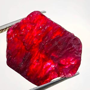 Puede incluir: Una gran gema de rubí rojo intenso con un acabado rugoso y natural. El rubí se sujeta con unas pinzas y tiene una apariencia translúcida.