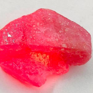 May include: A large, pink, rough-cut gemstone with a translucent, glassy finish. The gemstone has a slightly irregular shape and appears to be wet.