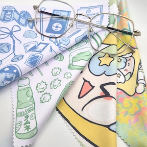 Può includere: Un paio di occhiali con montatura argentata poggia su diversi panni per la pulizia in microfibra colorati. I panni presentano vari disegni di cartoni animati, tra cui un rotolo di pellicola, un lettore musicale e una bottiglia di soda giapponese. I panni sono bianchi, blu, gialli e verdi.