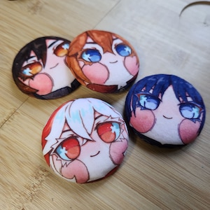 Pode incluir: Quatro botões redondos de pelúcia com rostos de desenhos animados. Cada botão apresenta um personagem diferente com cabelo e olhos de cores diferentes. Os personagens têm bochechas rosadas e sorriem.