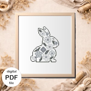 May include: A framed cross-stitch pattern of a rabbit filled with floral designs in shades of gray. The artwork is in a light wooden frame. The words "digital PDF file" are in a white circle in the lower left corner.