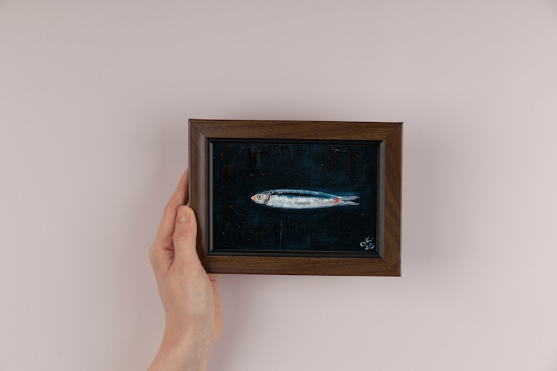 May include: A framed painting of a silver fish on a dark blue background. The painting is in a dark brown frame and has the signature 'OK 23' in the bottom right corner. Sardine art original painting Sardines still life oil painting miniature Anchovy fish painting French country kitchen art 4x6