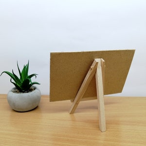 May include: A small, brown cardboard sign with a wooden easel stand. The sign is blank and ready for a message.