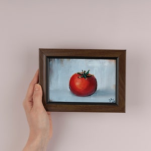 May include: A framed painting of a red tomato on a white background. The painting is signed "D.K. 2022" in the bottom right corner.