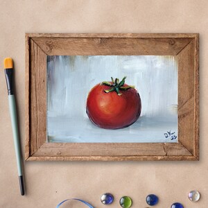 May include: A framed oil painting depicting a single red tomato on a white background. The tomato has a green stem and leaves. The painting is signed "D.K. 23" in the bottom right corner.