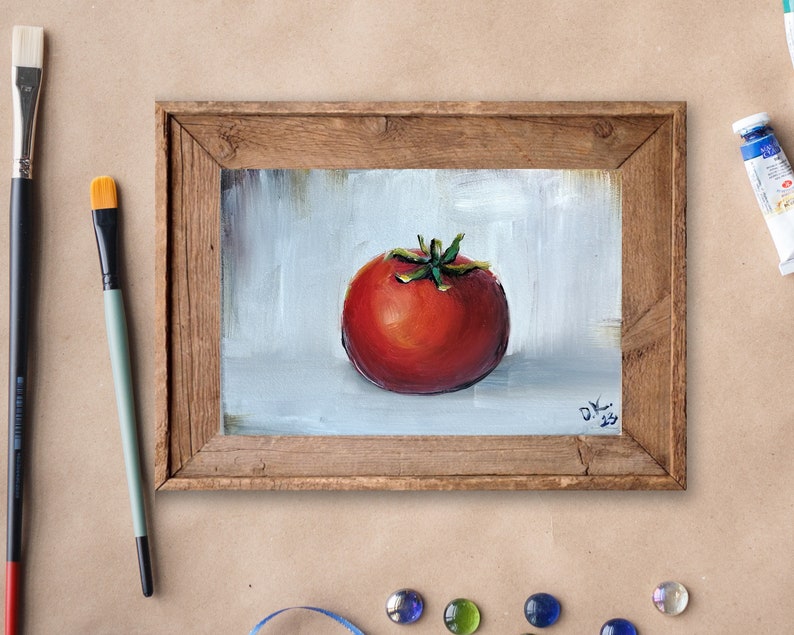 May include: A framed oil painting depicting a single red tomato on a white background. The tomato has a green stem and leaves. The painting is signed "D.K. 23" in the bottom right corner.