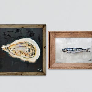 May include: Two framed paintings. One features a detailed oyster shell on a dark background. The other depicts a fish on a light background. Both paintings are in rustic wooden frames, adding a touch of natural charm to the artwork.