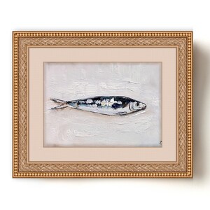 May include: Oil painting of a fish in a gold frame. The fish is painted in shades of blue, white, and black against a textured white background. The frame is ornate with a gold finish. The artwork is a still life.