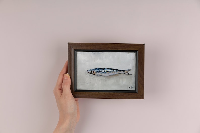 May include: A framed painting of a single, silver-colored fish with blue and black markings on a white background. The frame is dark brown wood.