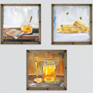 May include: Three framed paintings depicting honey-related scenes. One shows a jar of honey with a dipper, another features honeycomb with bees, and the last shows a honey dipper and jar. The paintings have a rustic, warm color palette.