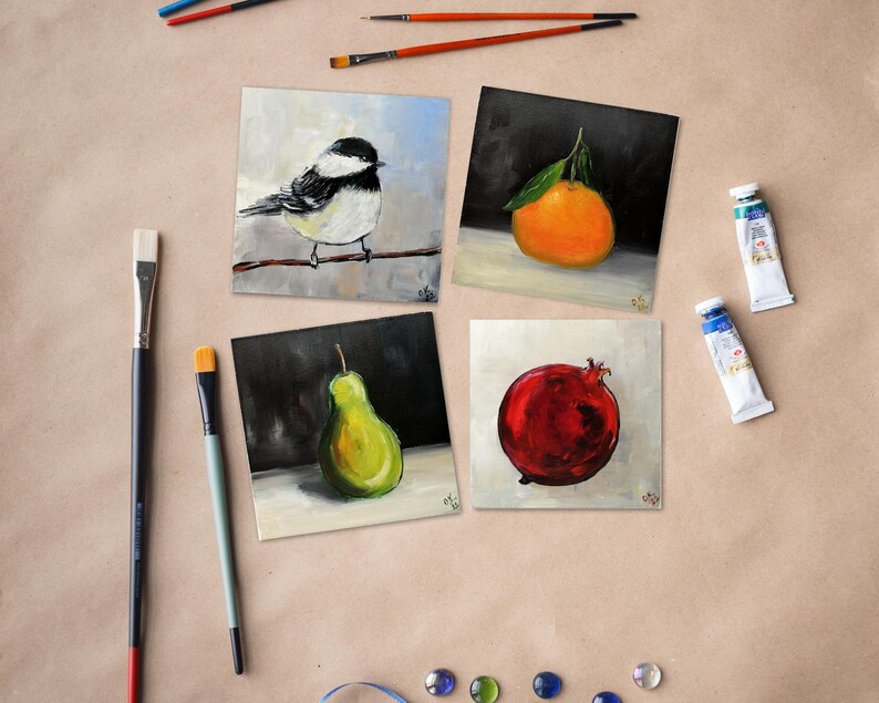 May include: Four square paintings of fruit and a bird, with paint tubes and brushes. The paintings depict a bird on a branch, an orange with a leaf, a green pear, and a red pomegranate. The art supplies are scattered around the paintings.