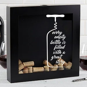 May include: Black wooden box with a glass front, filled with wine corks. The box has a white silhouette of a wine bottle and corkscrew with the text "every empty bottle is filled with a great story".