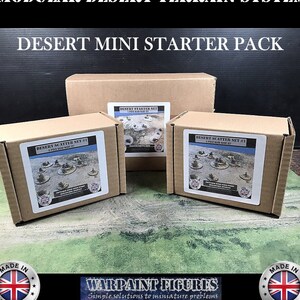 May include: Three cardboard boxes containing a desert terrain starter pack for miniature wargaming. The boxes are labeled "Desert Scatter Set #1" and "Desert Starter Set".